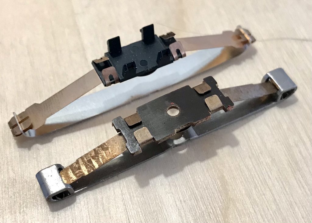 Two Märklin sliders removed from locomotives: long metal strips with raised ends and a mounting plate in the middle